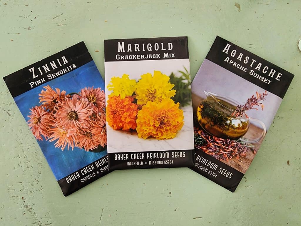 Image of pink Zinnia, Marigold, and Agastache flower seed packets on greed rustic background