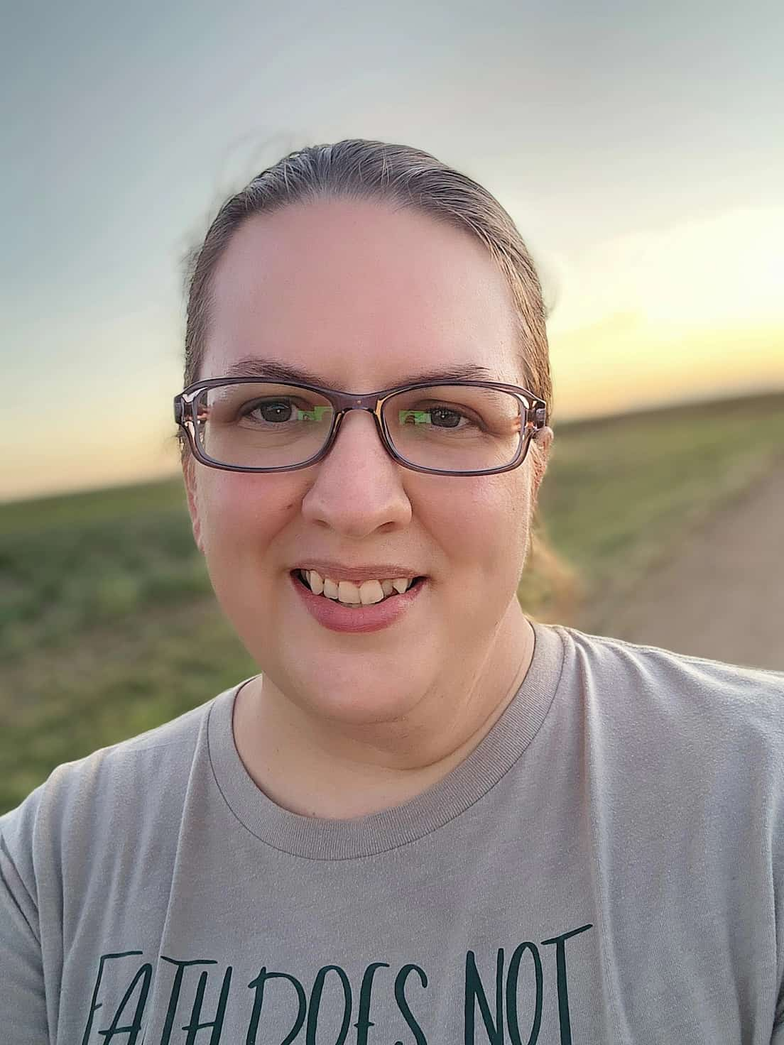 an image of Rachel (a woman with brown hair) taking a selfie with a pasture and beautiful sunset in the background